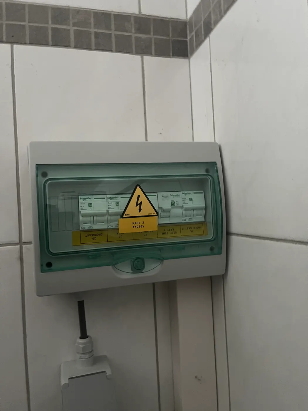 Kleine verdeelkast met transparant deksel op betegelde muur, geplaatst door Wattra