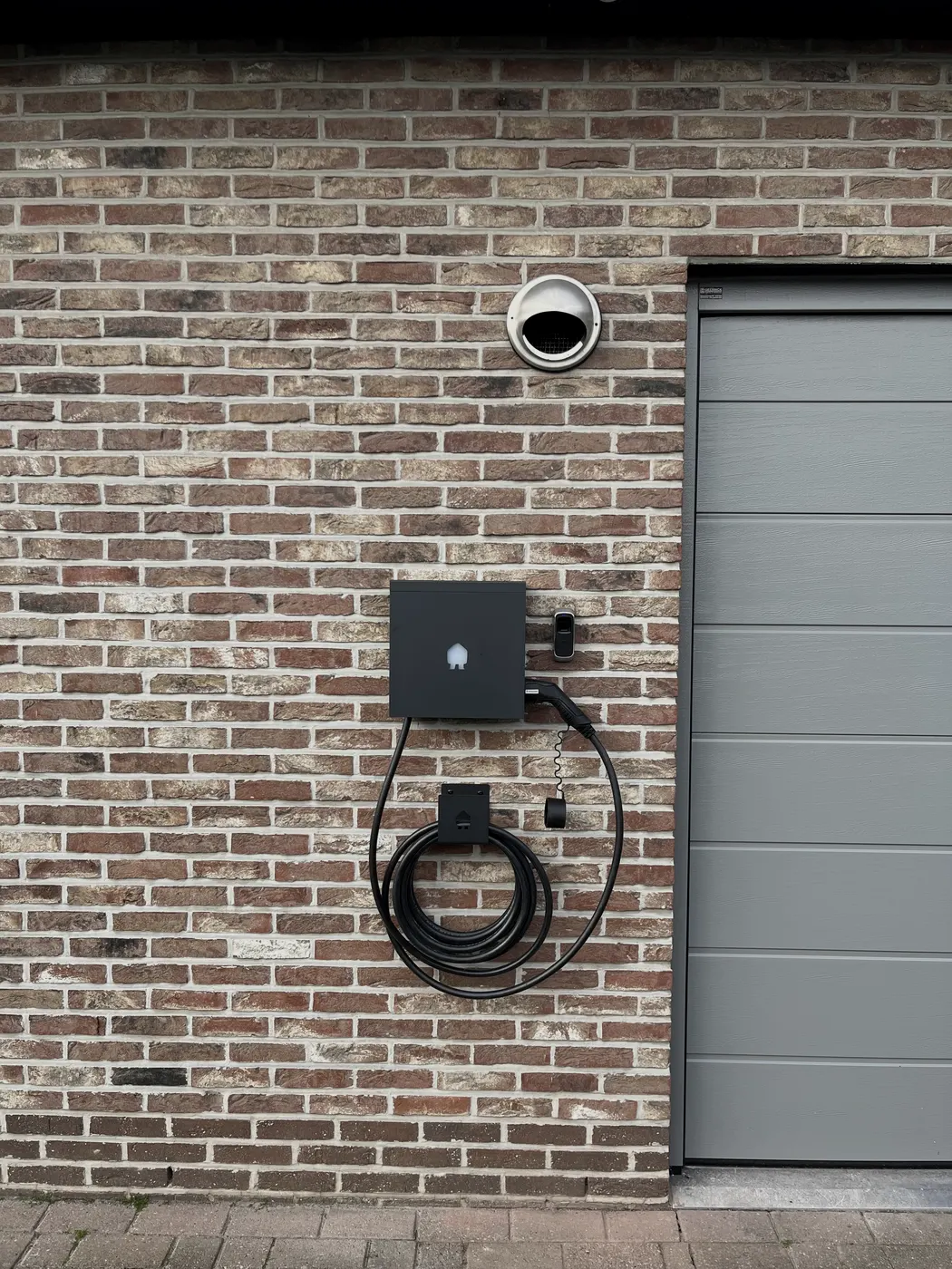 zwarte laadpaal met kabel naast garagepoort, geplaatst door Wattra