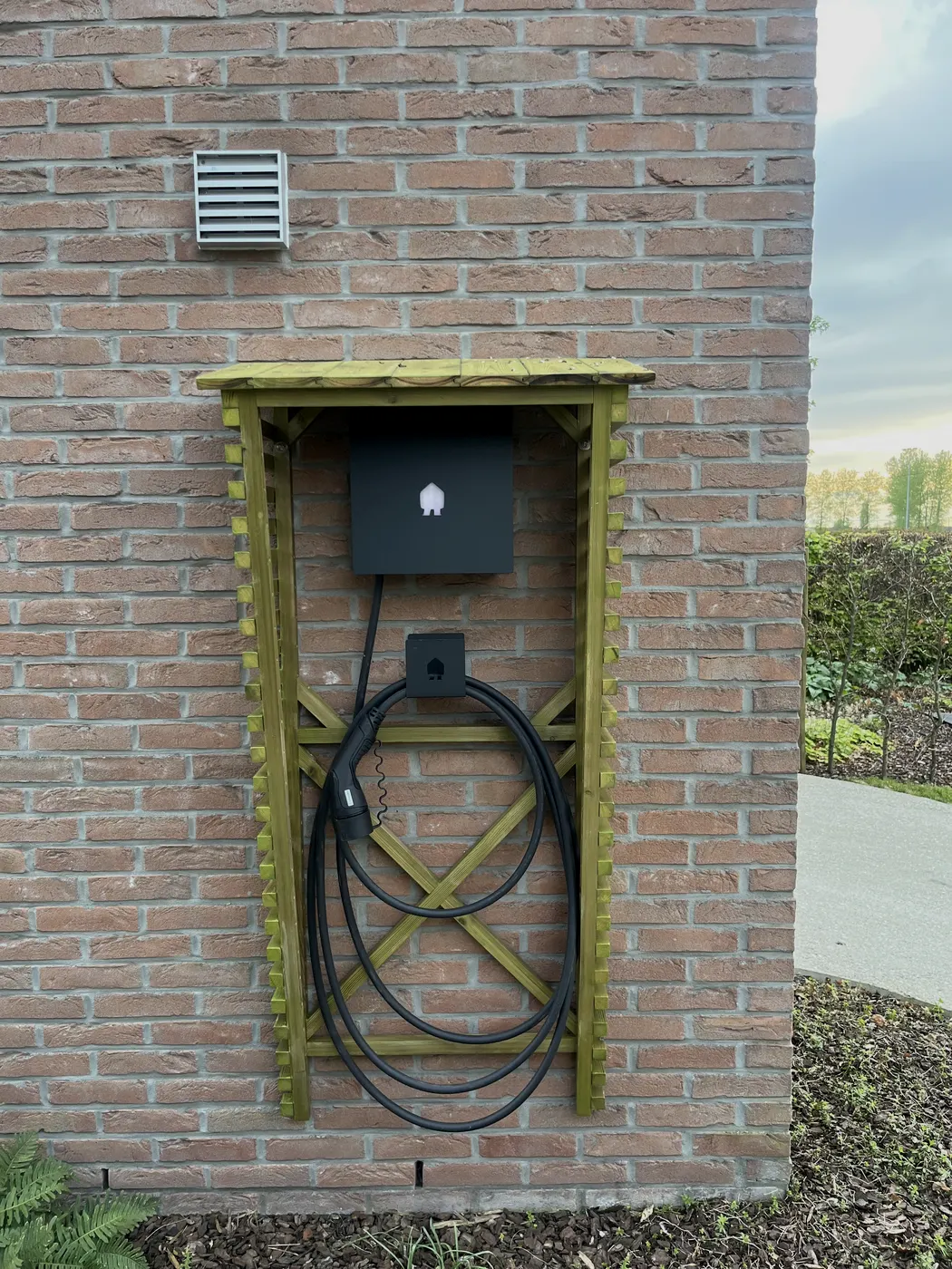 laadpaal in houten kader tegen gevel, geplaatst door Wattra