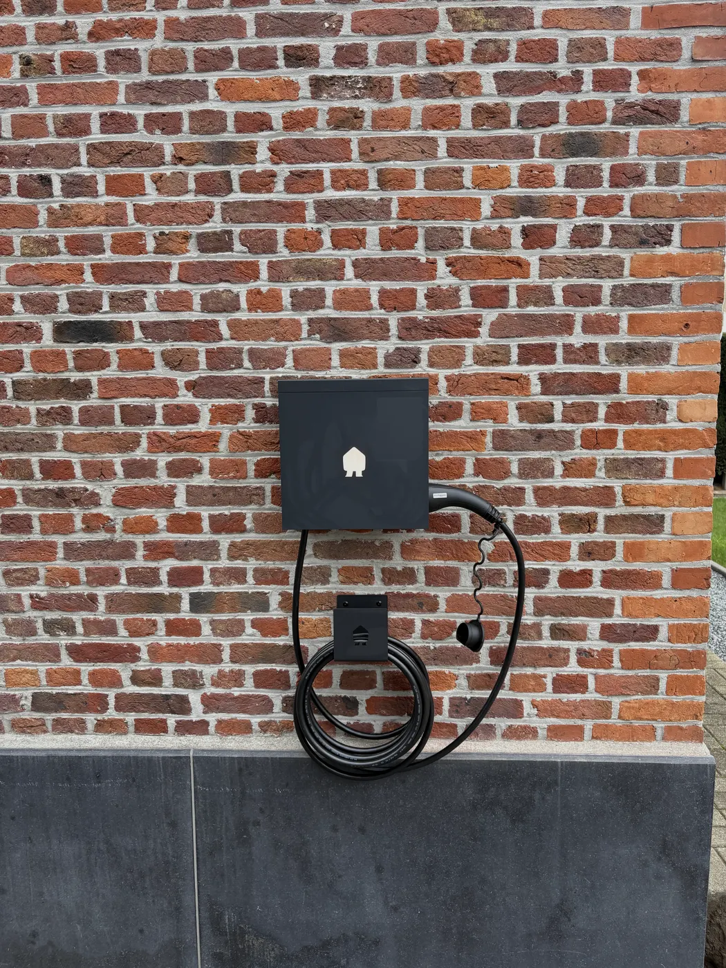 Zwarte Smappee met opgerolde kabel, mooi gecentreerd op gevel, geplaatst door Wattra