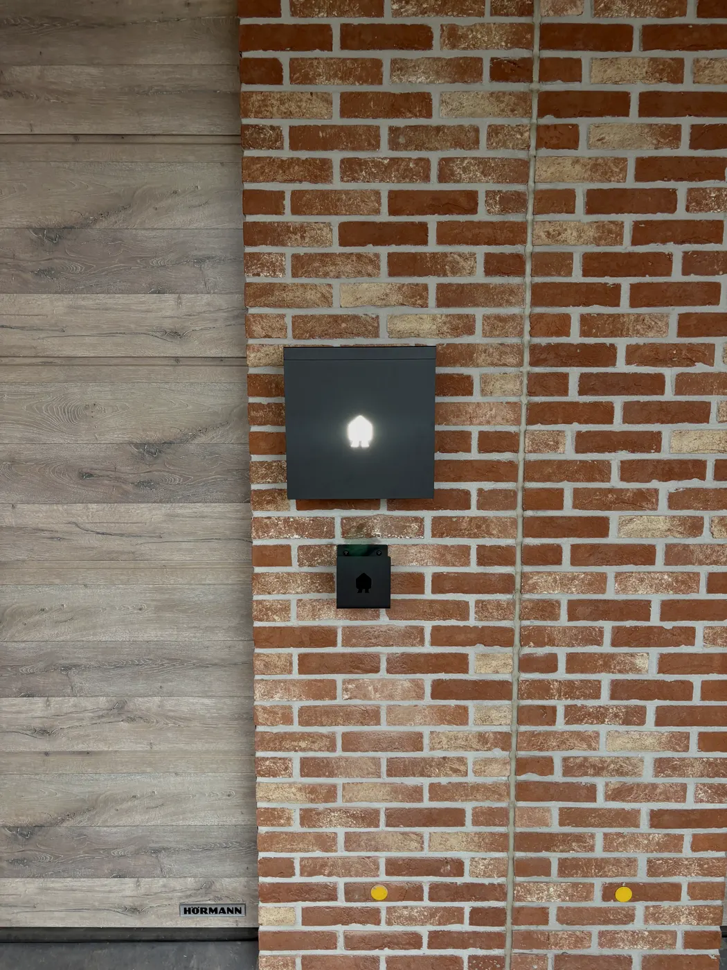 Antraciet Smappee op rustieke gevel naast houten poort, geplaatst door Wattra