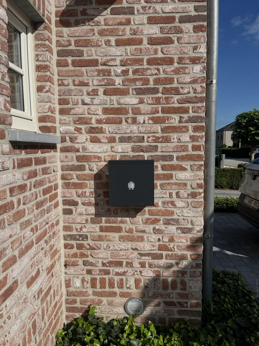 laadpaal op bakstenen hoekgevel met blauwe lucht, geplaatst door Wattra