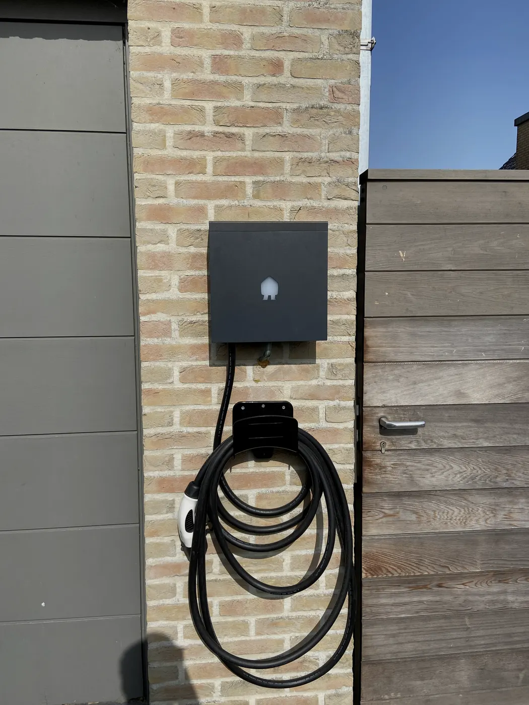 Zwarte Smappee laadpaal op gevel met opgerolde kabel, geplaatst door Wattra