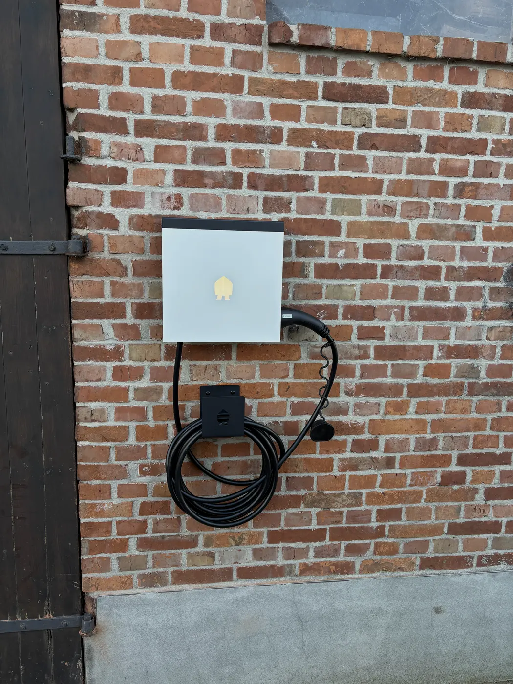 Witte Smappee wallbox met opgerolde kabel op baksteen, geplaatst door Wattra