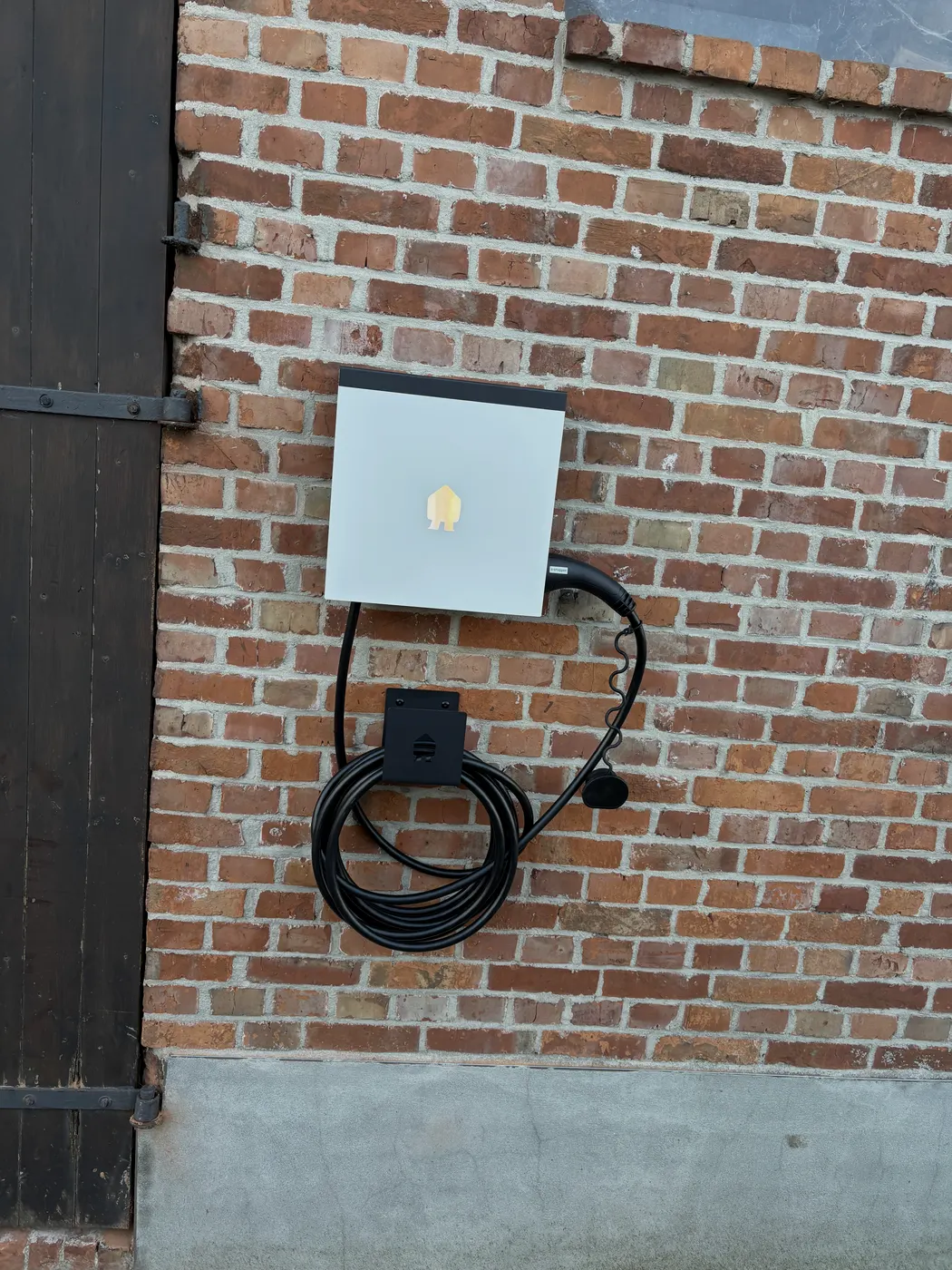 Witte Smappee laadpaal met kabel op bakstenen gevel, geplaatst door Wattra