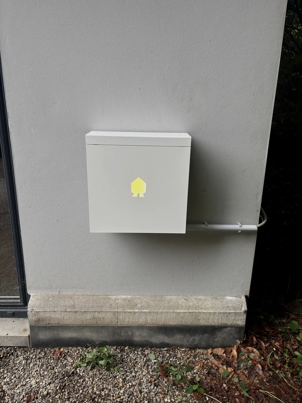 Witte Smappee laadpaal met oplichtend logo op gevelhoek, geplaatst door Wattra