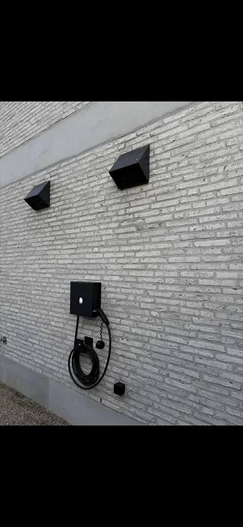 Zwarte laadpaal en buitenlampen op witte bakstenen gevel, geplaatst door Wattra