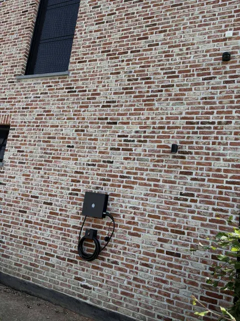 Zwarte wallbox met laadkabel op mooie bakstenen gevel, geplaatst door Wattra