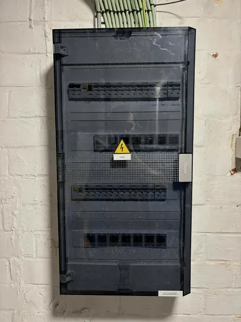 Donkere verdeelkast netjes gemonteerd op witte keldermuur, geplaatst door Wattra