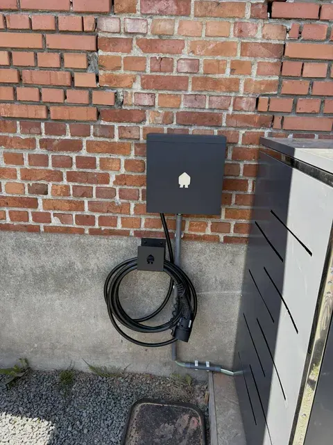 Zwarte Smappee laadpaal op rode bakstenen muur bij carport, geplaatst door Wattra