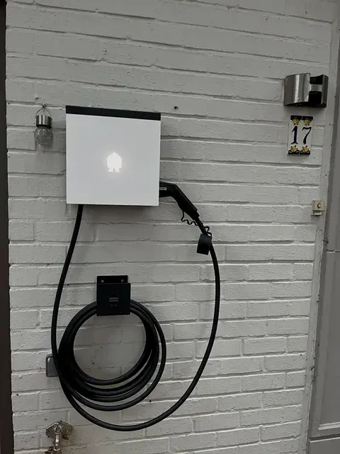 Witte Smappee laadpaal met kabel op witte baksteenmuur, geplaatst door Wattra