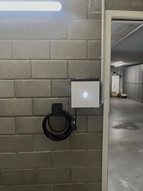 Laadpaal met verlicht huisje-logo in parkeergarage, geplaatst door Wattra