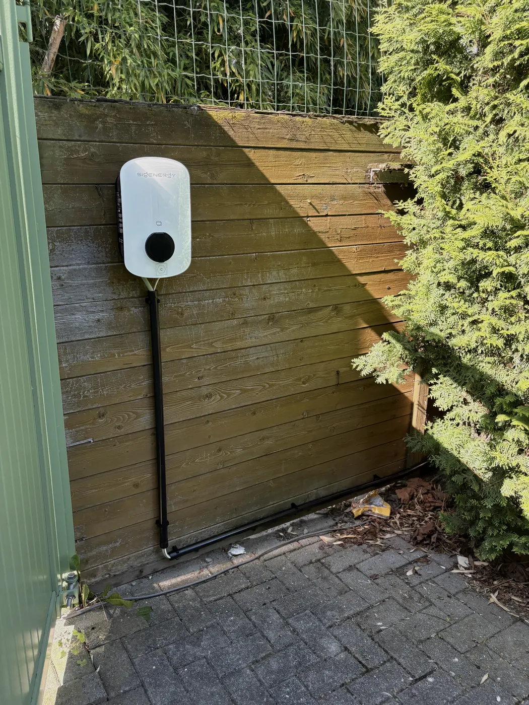 Witte wallbox op houten schutting naast haag, geplaatst door Wattra
