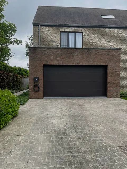 Woning met laadpaal naast donkere garagepoort, geplaatst door Wattra