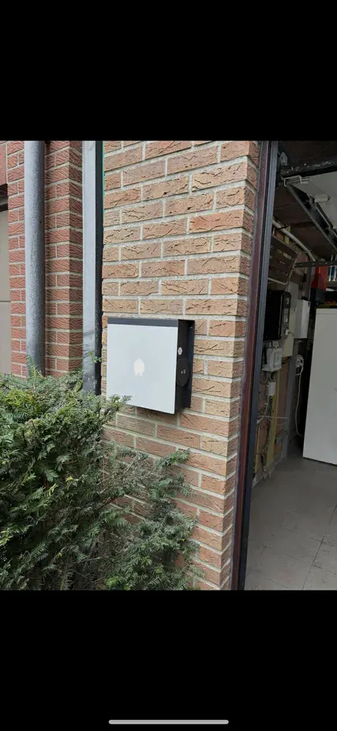 Witte wallbox op bakstenen muur bij doorgang, geplaatst door Wattra
