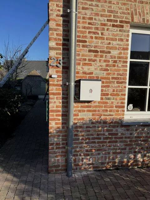 Wit toestel op bakstenen gevel bij huisnummer, ladder achteraan, geplaatst door Wattra