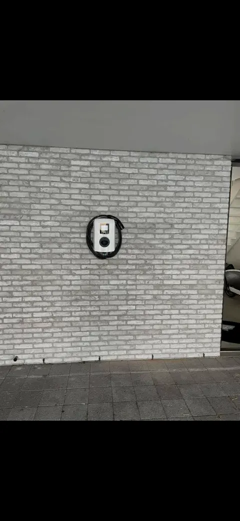 Witte Alfen laadpaal met opgerolde kabel op witte bakstenen gevel, geplaatst door Wattra