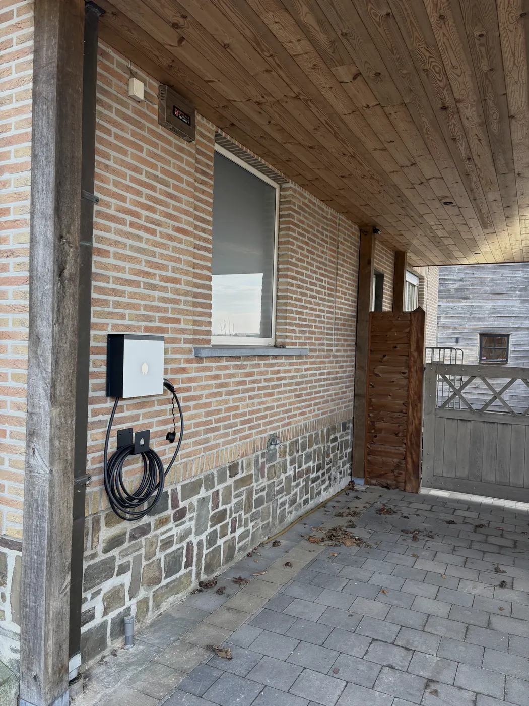 witte wallbox onder houten carport aan gevel, geplaatst door Wattra