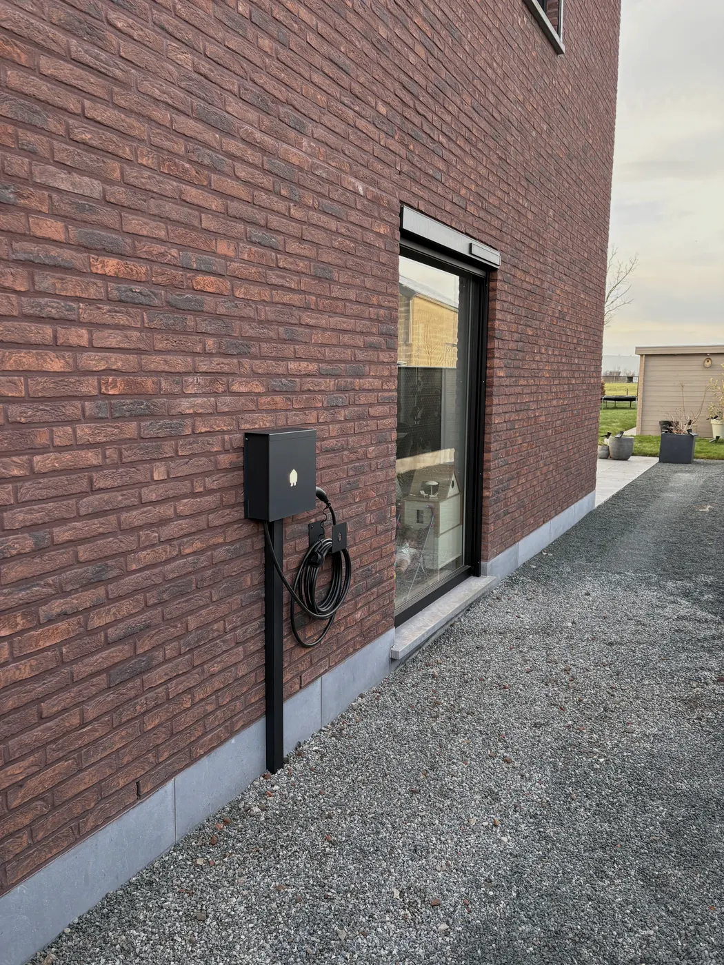 zwarte wallbox op staander naast raam, nieuwbouwwoning, geplaatst door Wattra